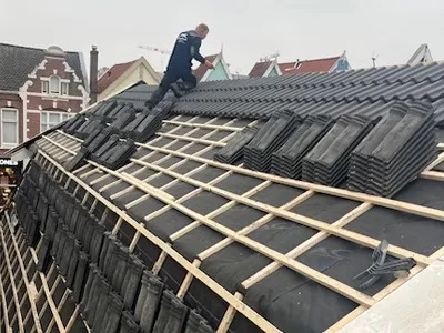 Dakdekker van Loodgieteramsterdam.eu voert een dakreparatie uit en legt nieuwe dakpannen op een dak in Amsterdam.