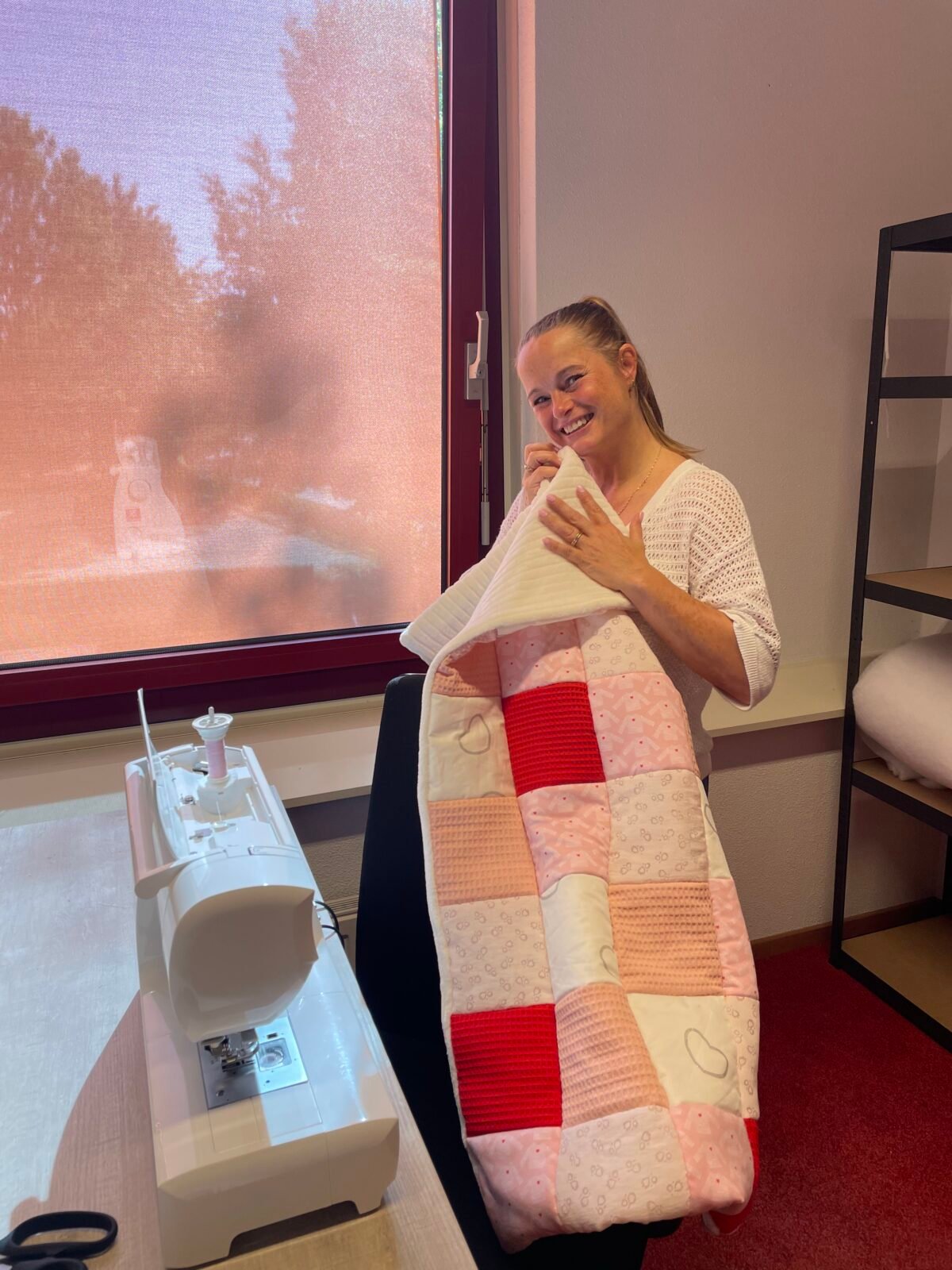 Een vrouw in het atelier van Stof vol Verhalen toont een handgemaakte herinneringsdeken met een naaimachine op de voorgrond